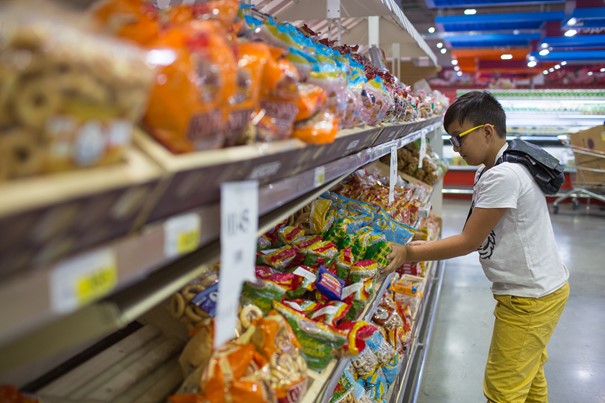 Jongen in supermarkt bij schappen met ongezonde snacks