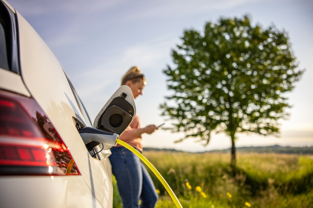 Vrouw kijkt op telefoon tijdens opladen auto in groen landschap
